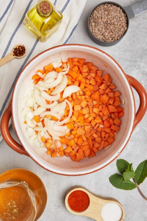 Diced carrots and onions in a ceramic baking dish for cooking or roasting.