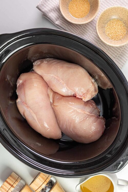 Raw chicken breasts in a slow cooker for easy shredded chicken recipes.
