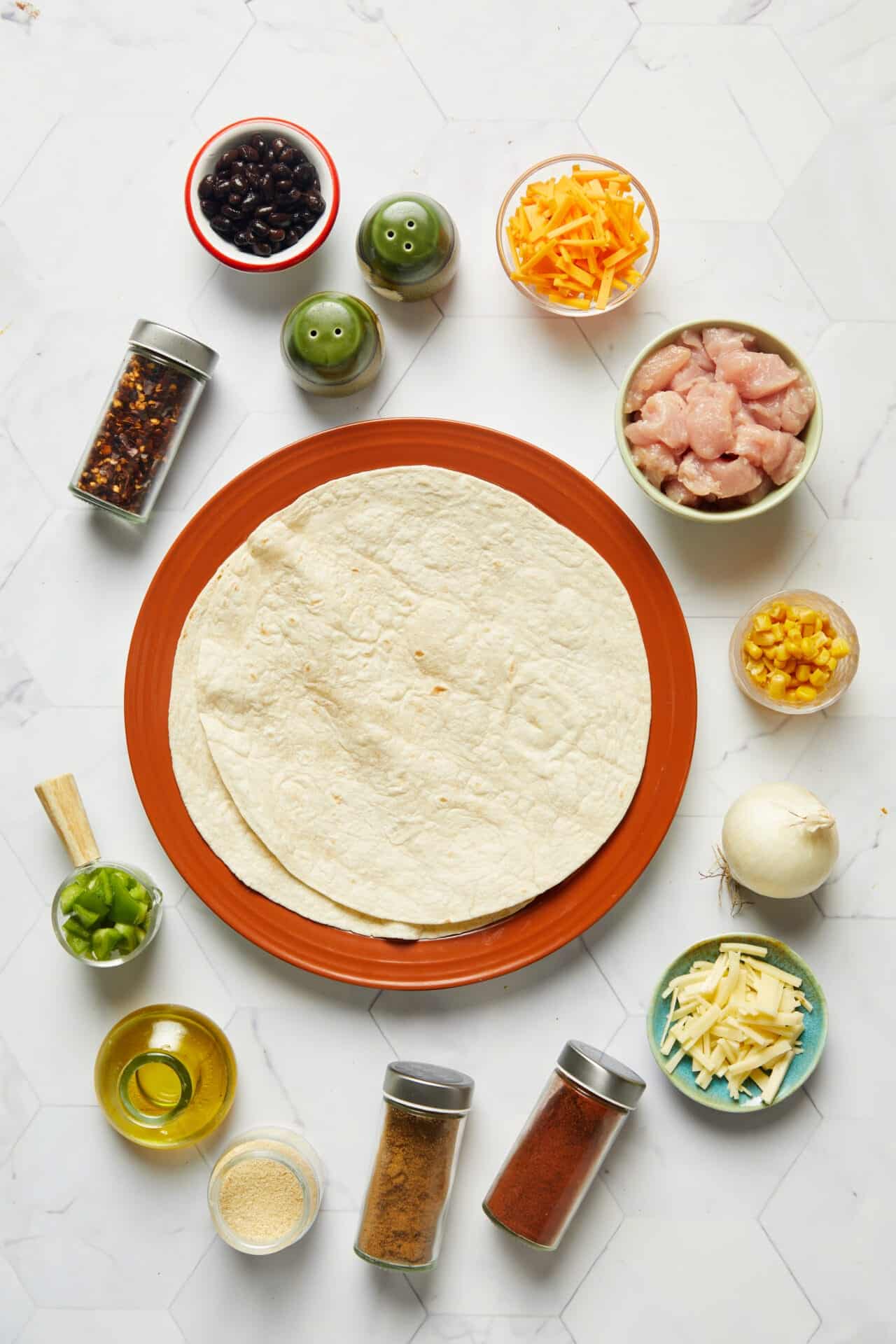 Fresh homemade chicken enchiladas ingredients with tortillas, cheese, chicken, and salsa on a white marble background.