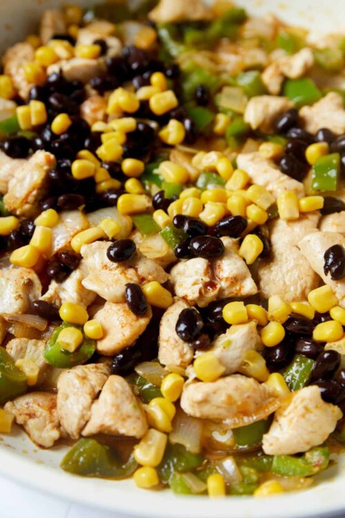 Sautéed chicken with black beans, corn, and green peppers in a white bowl.