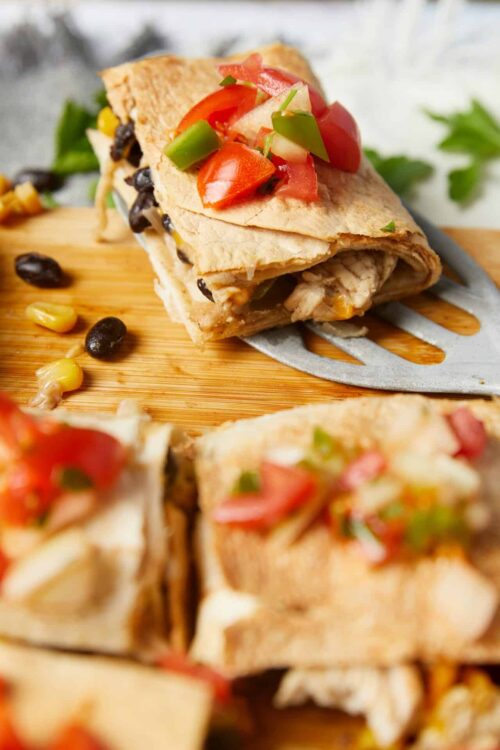 Fresh chicken fajita burrito wrapped in a tortilla with melted cheese, black beans, and colorful toppings, served on a wooden cutting board.