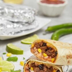 Baked beef burrito cut in half showing meat, corn, beans, and rice inside.