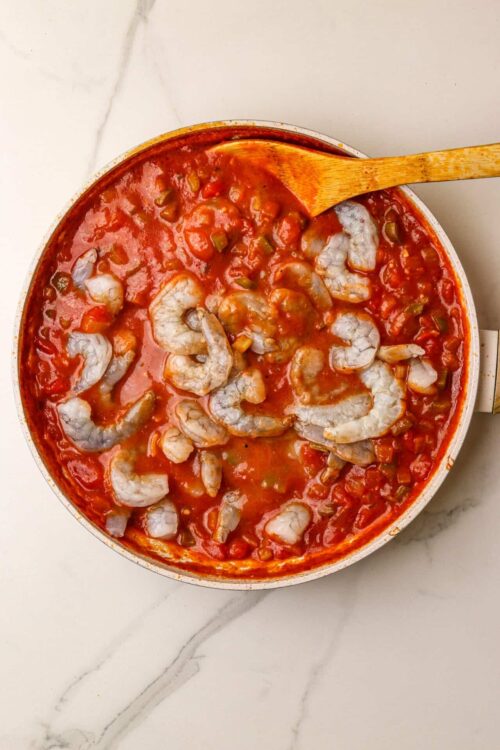 Creamy shrimp and tomato stew in a white skillet with a wooden spoon.