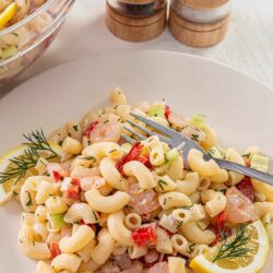 Creamy shrimp pasta salad with lemon and fresh herbs on a white plate.