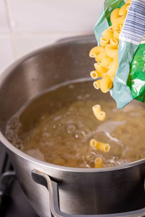 Uncooked pasta being added to boiling water in a stainless steel pot.