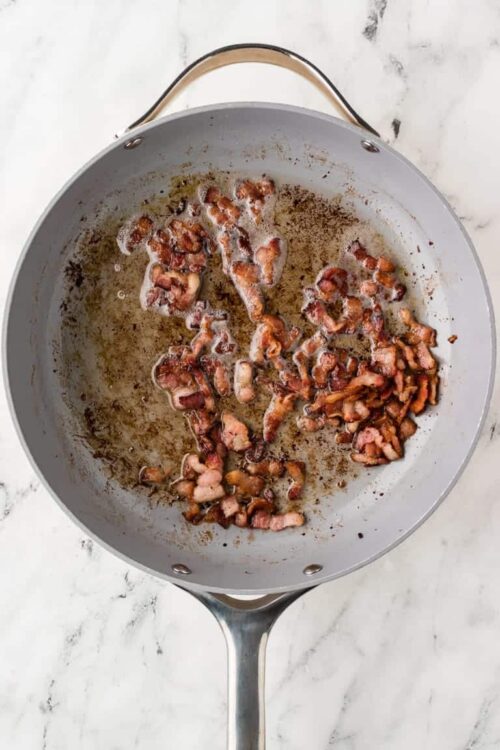 Crispy cooked bacon in a skillet on a marble countertop, ready for breakfast or recipes.