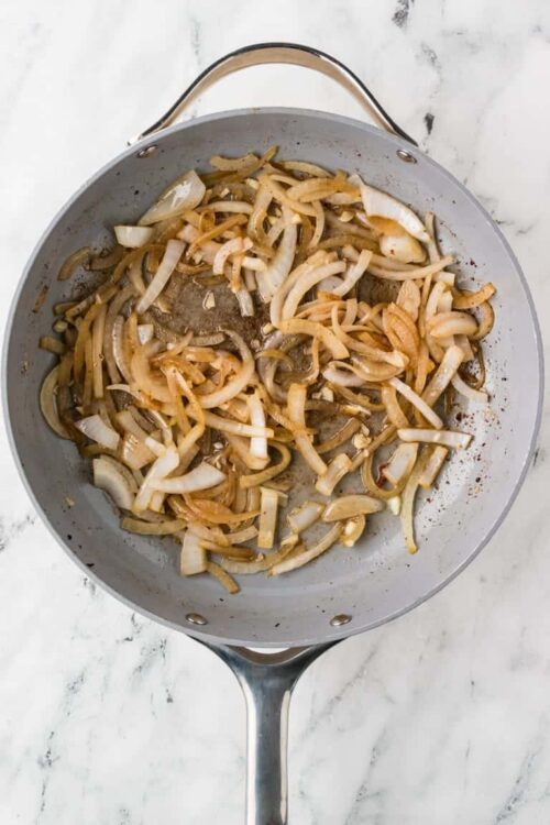 Cooked sautéed onions in a stainless steel skillet for caramelization and flavor.