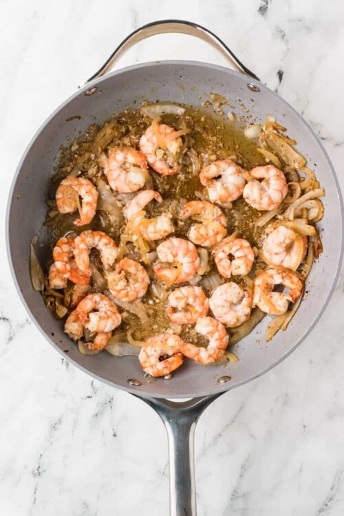 Cooked shrimp with sautéed onions in a skillet.