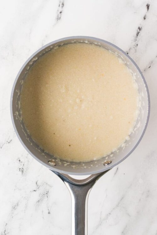 Creamy sauce simmering in a stainless steel saucepan on a marble countertop, perfect for baking and cooking recipes.