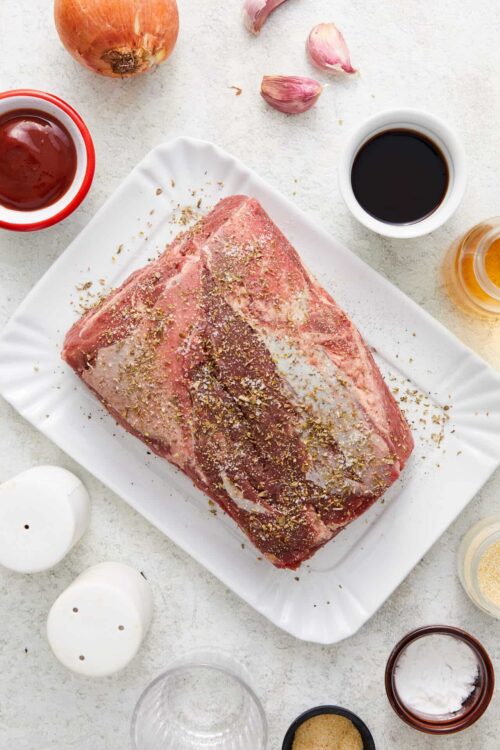 Juicy beef brisket with seasonings and condiments ready for roasting.