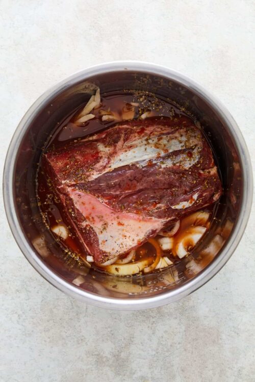Marinated beef brisket with soy sauce and garlic in a metal bowl.