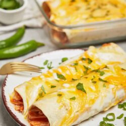 Cheesy beef enchililladas with melted cheese and chopped green onions on a white plate.