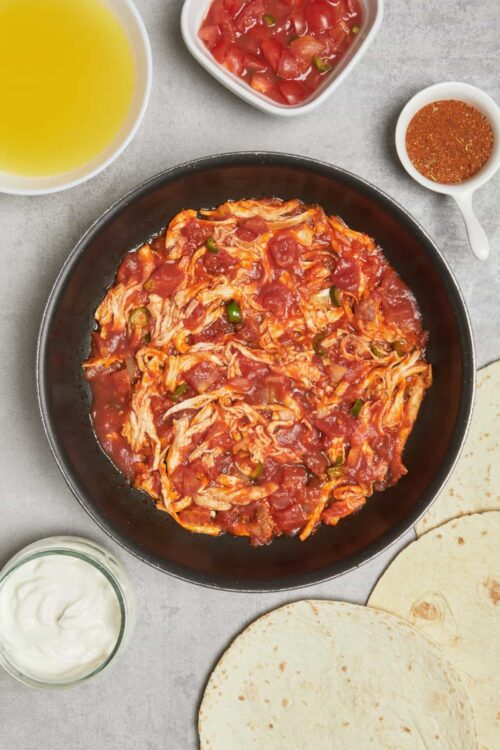Savory shredded chicken chili with tomatoes in a black skillet.