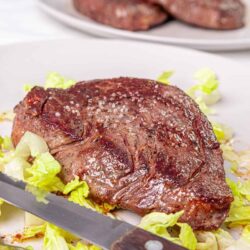 Juicy grilled steak on a white platter with fresh lettuce, ready to serve, perfect for steak recipes.