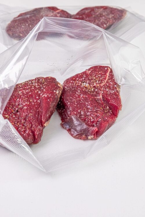 Vacuum-sealed raw steaks on a white surface for optimal freshness.