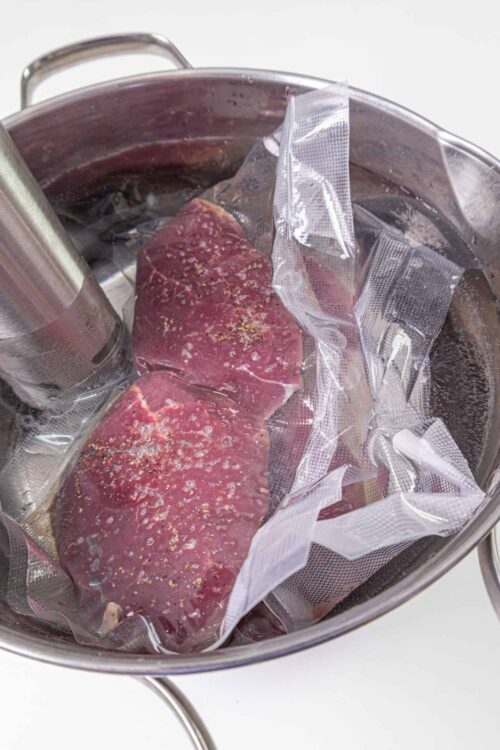Raw steak being vacuum sealed with a vacuum pump in a stainless steel container.