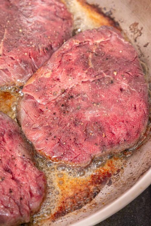 Juicy, seasoned beef steaks searing in a skillet with bubbling butter and spices. Perfect for a flavorful grilled or pan-fried meal.