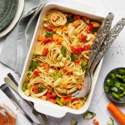 Vegetable fried rice in a white baking dish with colorful chopped vegetables and silver serving utensils.