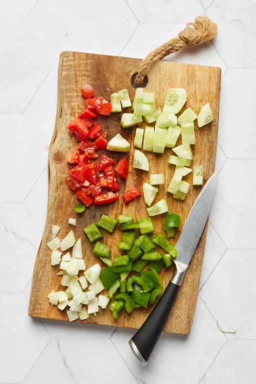 Chopped tomatoes, cucumbers, bell peppers, and onions on a wooden cutting board for cooking or preparing fresh salad.