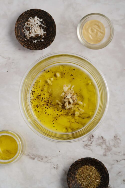 Olive oil, garlic, and herbs in a glass bowl for cooking recipes.