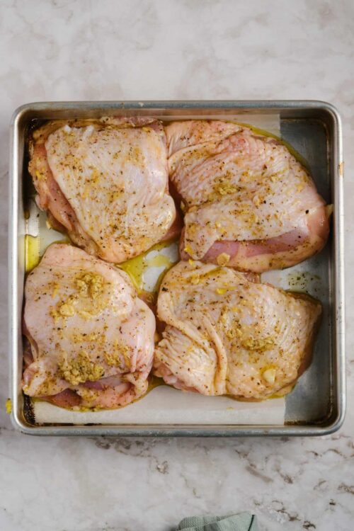 Baked chicken thighs seasoned with garlic and herbs in a metal baking pan.