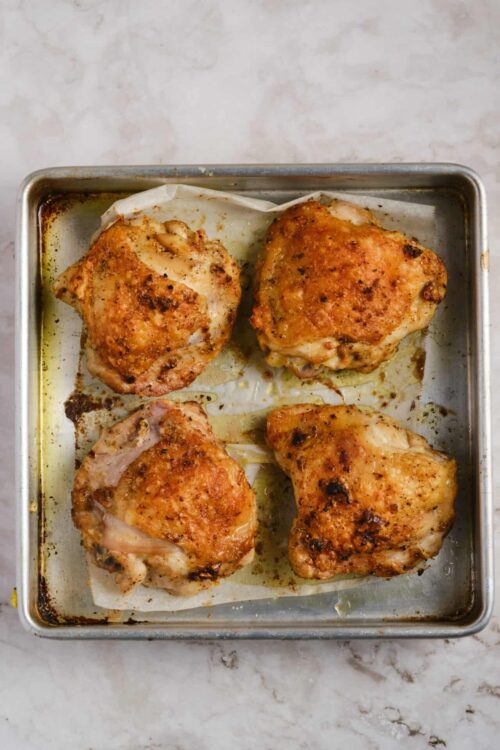 Crispy baked chicken thighs on a roasting pan with golden skin and seasoned crispy texture.