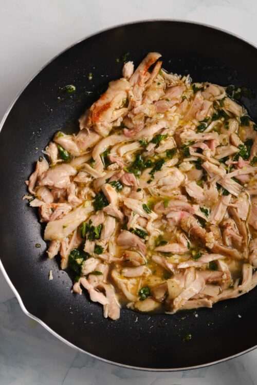 Crispy shredded chicken in a skillet with herbs and garlic for easy recipes.