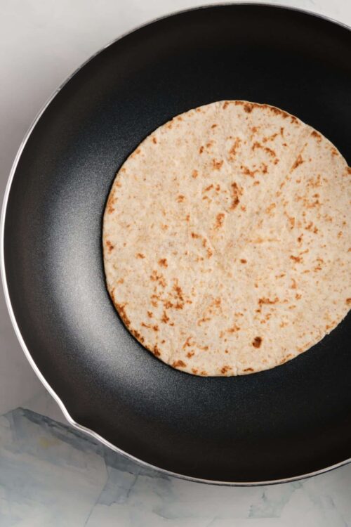 Crispy flour flatbread cooking in non-stick skillet.