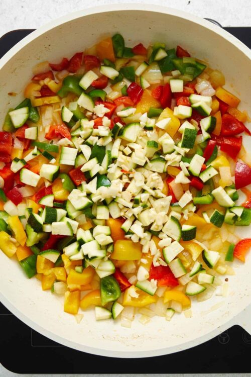 Chopped colorful bell peppers and garlic in a skillet for a vegetable stir-fry or recipe preparation.