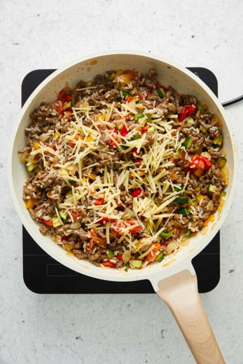 Savory ground beef and vegetable stir-fry in a white skillet on a stovetop.