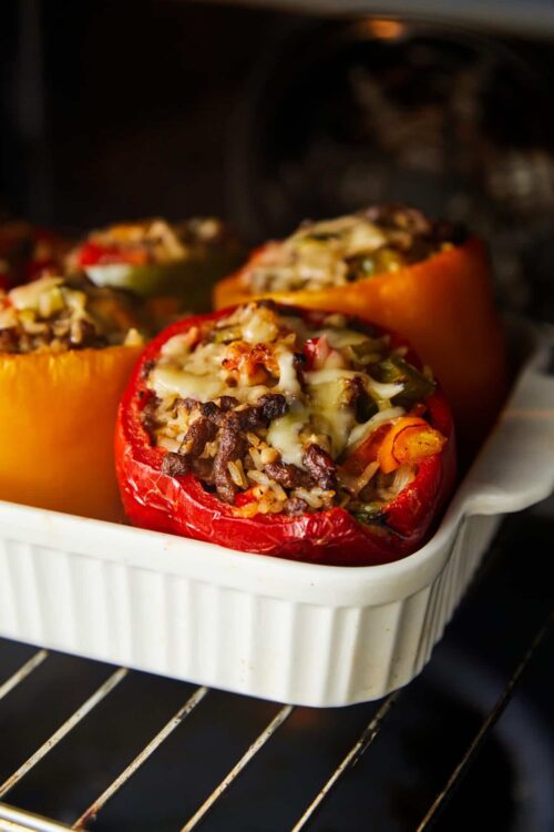 Colorful stuffed bell peppers baking in oven, topped with melted cheese.