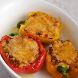 Colorful stuffed bell peppers with melted cheese in a white baking dish.