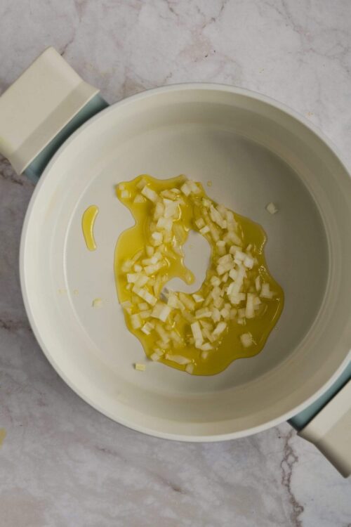 Minced onions and olive oil in a white slow cooker for cooking or sautéing.