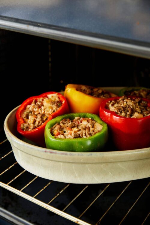 Stuffed bell peppers with rice, beef, and vegetables baking in oven.