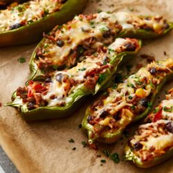 Stuffed bell peppers filled with seasoned ground meat, black beans, corn, and melted cheese on a parchment-lined baking sheet.