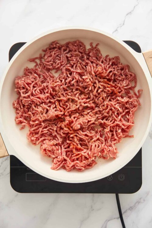 Ground beef cooking in a white skillet on an electric stove.