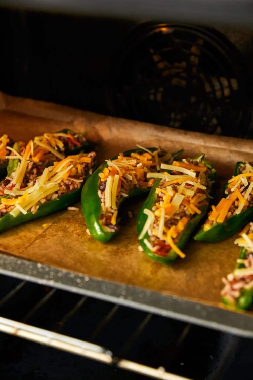 Green bell peppers stuffed with rice, ground meat, and shredded cheese baking in the oven.