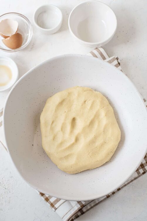 Soft peeled dough resting on a white speckled plate, ready for baking bread or pastry.