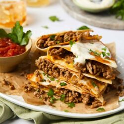 Savory beef and cheese quesadillas with fresh herbs on a white plate.