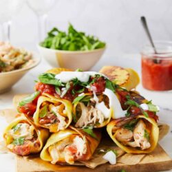 Delicious chicken and vegetable egg roll wraps on a wooden board with fresh toppings.