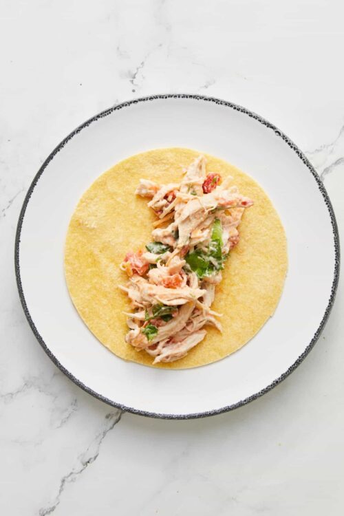 Shredded chicken and vegetable filling on a yellow corn tortilla, ready to be rolled for tacos.