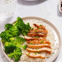 Steamed chicken with broccoli over rice, garnished with sesame seeds, on a plate for Asian-inspired dinner.