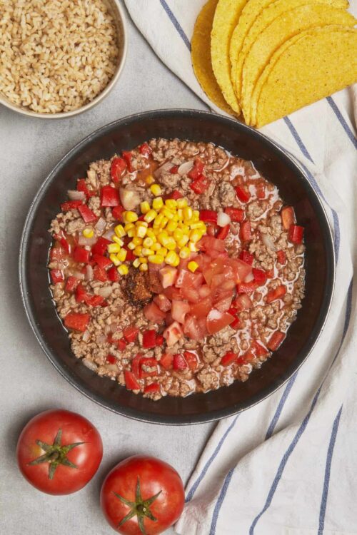 Savory taco filling with ground beef, tomatoes, corn and spices in a black skillet.
