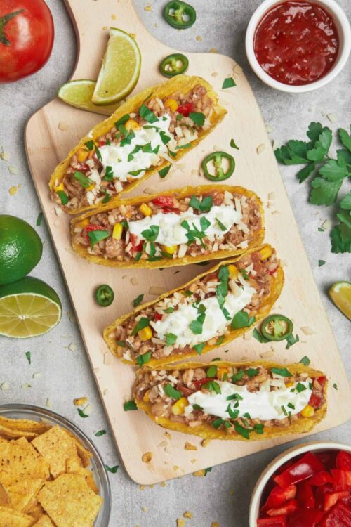 Savory ground beef taco salads in taco shells topped with sour cream and fresh herbs on a wooden serving board.