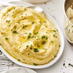 Creamy mashed potatoes garnished with chopped fresh parsley, served on a white dish.