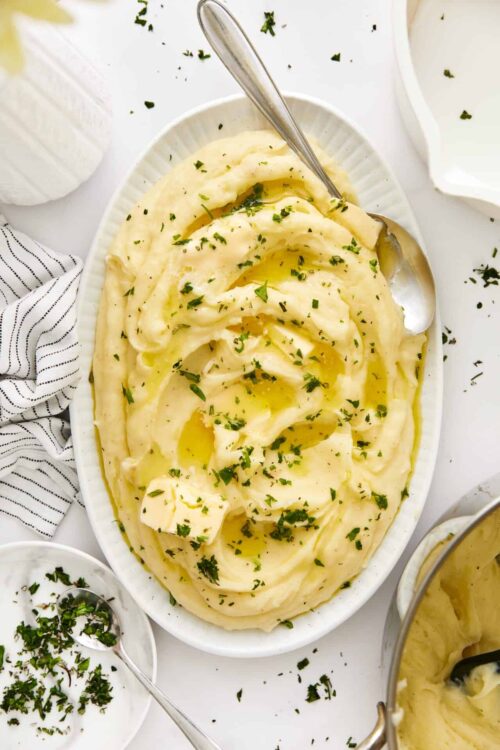 Creamy mashed potatoes with butter and herbs, served in a white oval dish.