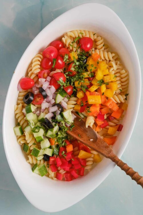 Colorful pasta salad with fresh vegetables and herbs on white serving dish.