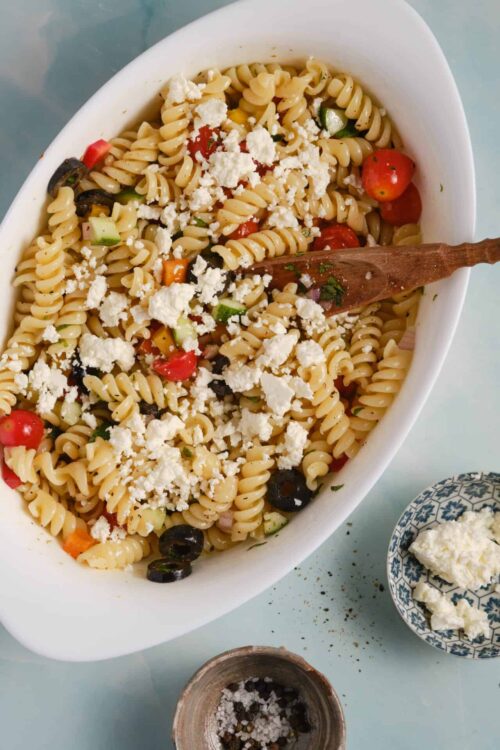 Creamy pasta salad with vegetables and crumbled feta cheese, served in a white dish.