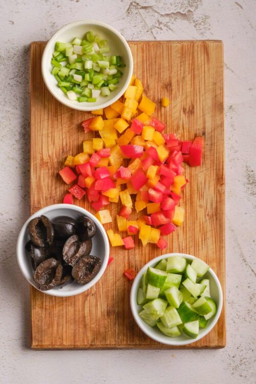 Colorful diced vegetables on a wooden cutting board for healthy cooking recipes.