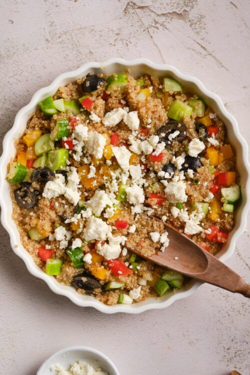 Colorful quinoa salad with vegetables and feta cheese in a white ceramic dish.